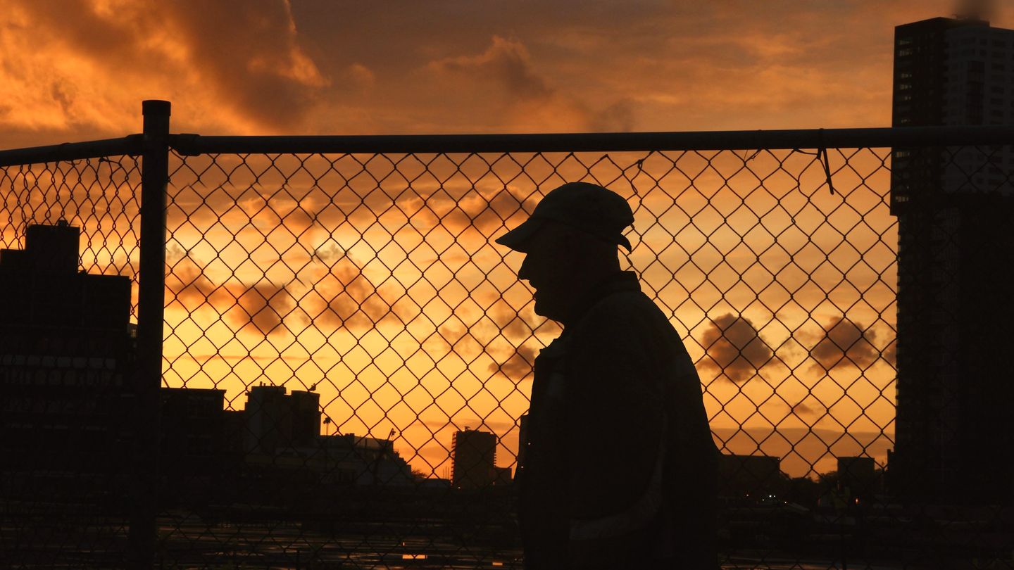 Illustrative image: a person silhouetted at a site fence against a sunset sky