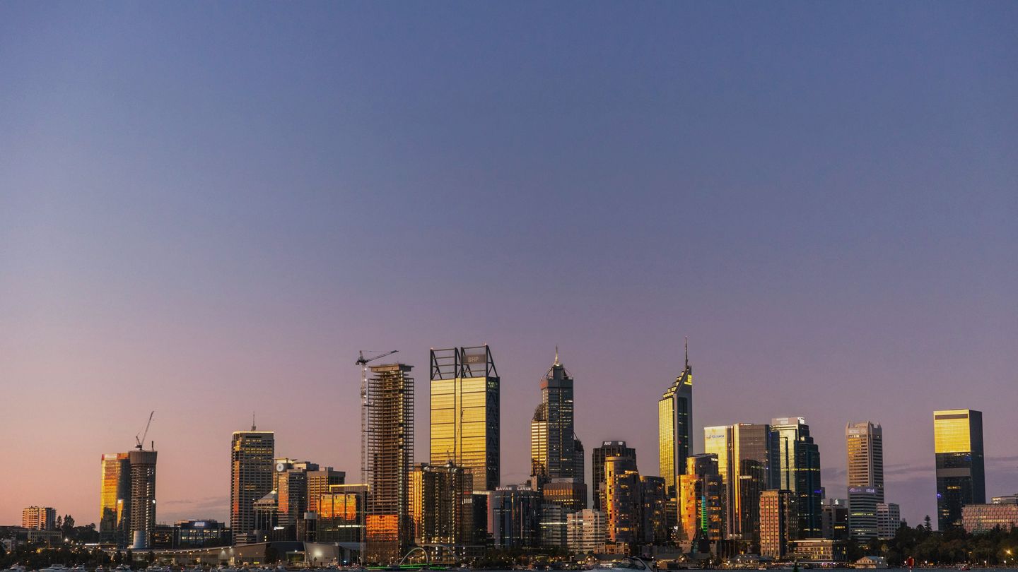 The Perth city skyline across the Swan River at dusk, towers lit gold by the last light